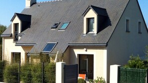Une maison à deux étages avec un toit en pente, de nombreuses fenêtres de toit et une entrée fermée par un portail.