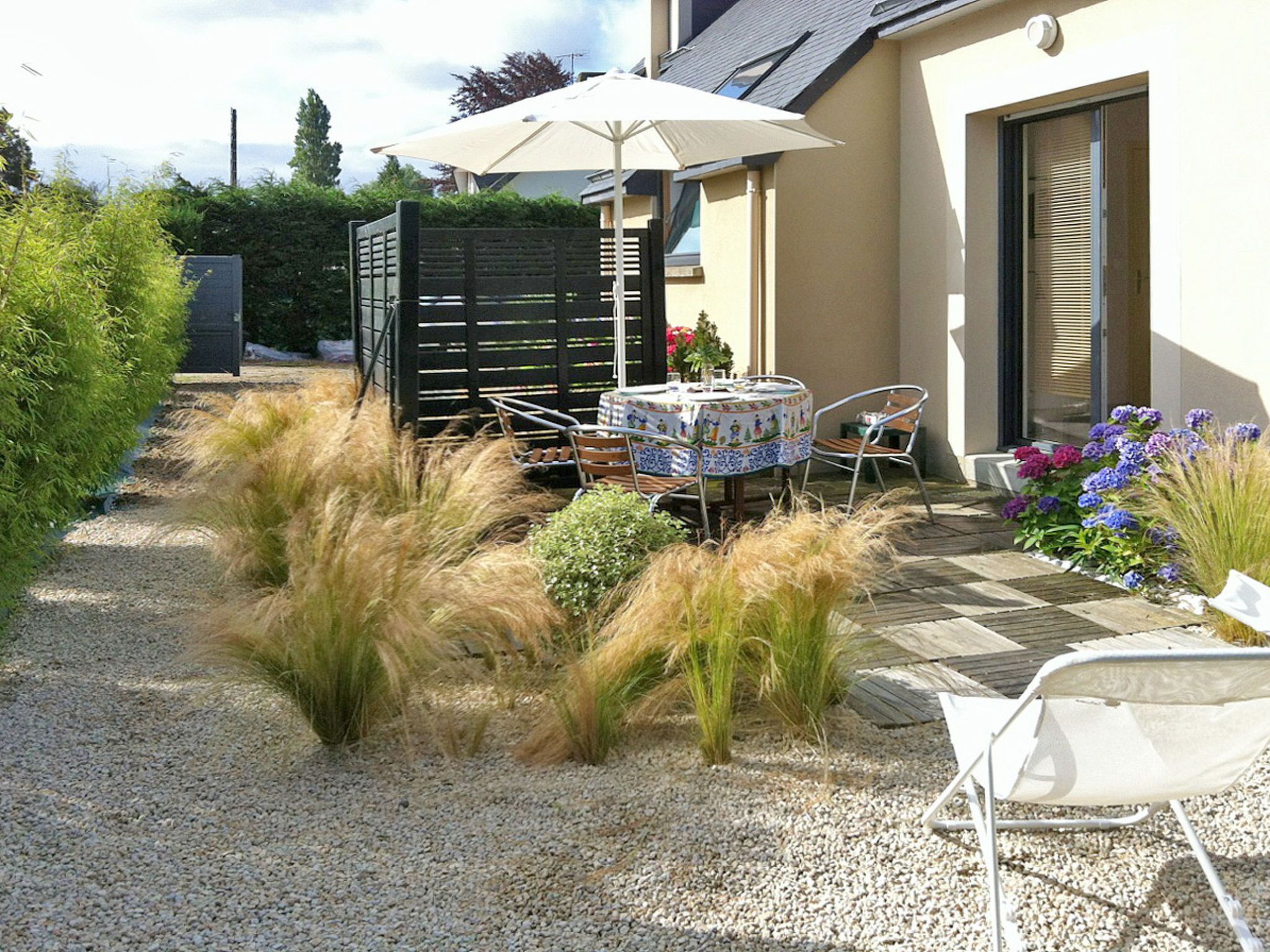 A patio area with a table and chairs, surrounded by decorative plants and a wooden fence.