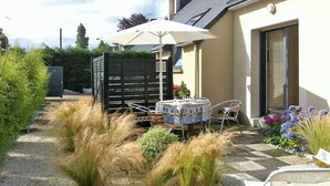 Un espace patio aménagé avec une table et des chaises, entouré de plantes décoratives et d’une clôture en bois.