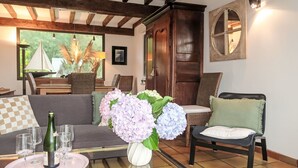 A living room with a sofa, chairs, a coffee table with wine glasses, a vase with flowers, and a view of the outdoors.