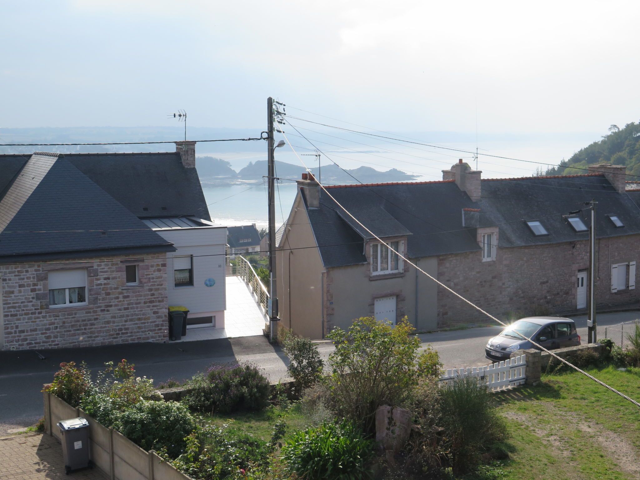Una strada residenziale con case, un'auto e vista sul mare.