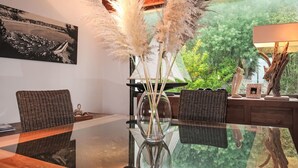 A dining area with a glass table, wicker chairs, a vase with pampas grass, and a painting on the wall.