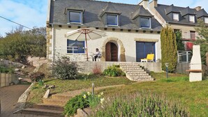 A two-story stone house with a balcony, a large umbrella, and a staircase leading to the entrance.