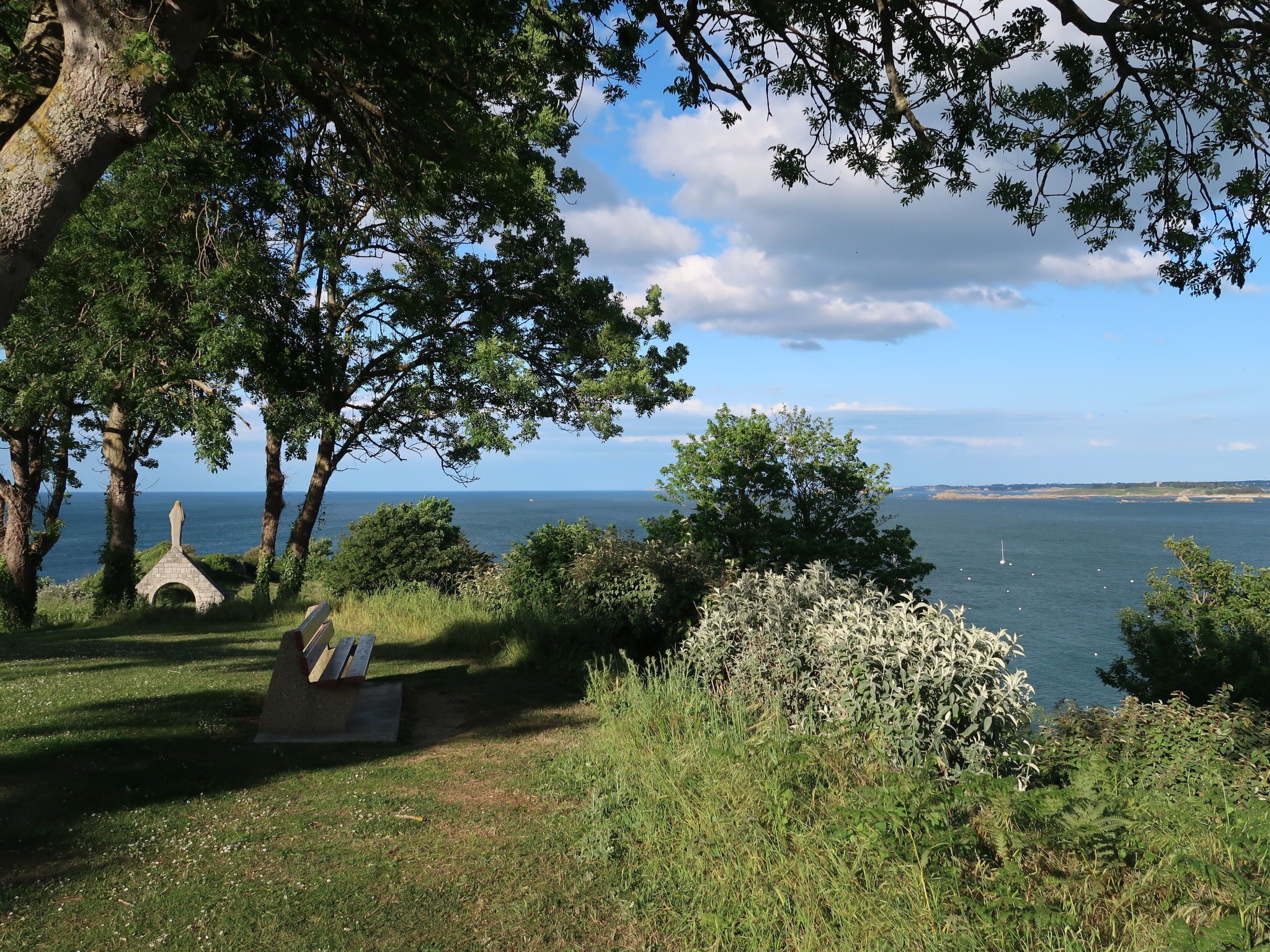 A park with a stone bench, trees, and a view of the sea.