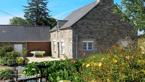 A stone building with a sloped roof, a satellite dish, and a garden with various plants and flowers. - L'Egven by Interhome (Saint Cast le Guildo)