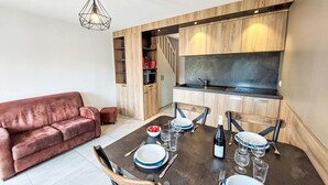 A modern kitchen with wooden cabinets, a dining table set for four, and a red sofa in the living area.