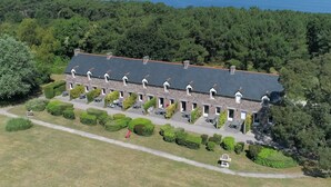 A large, rectangular building with a stone facade and multiple dormer windows. It is surrounded by well-maintained lawns and hedges, with a view of the sea in the background.