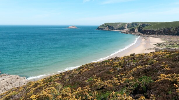A coastal landscape with a beach, rocky cliffs, and a distant island.