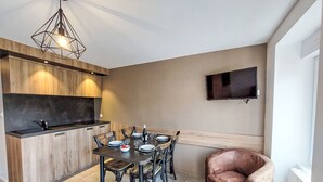 A modern kitchen with a dining area, a TV mounted on the wall, and a leather chair.