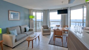 Una habitación de hotel moderna con balcón, sofá, mesa de comedor y televisor.