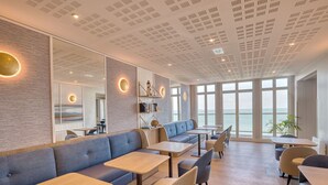 Un restaurante moderno con vista al mar, que ofrece diversas opciones de asientos, incluyendo sofás y mesas.