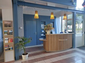 A reception desk with a potted plant, a wooden bookshelf with brochures, and a blue door.