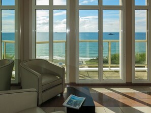 Quarto com uma janela ampla com vista para o mar, um sofá e uma pequena mesa com uma revista.