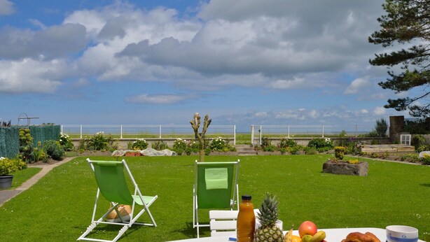 Mesa al aire libre con vista al mar, zona verde y valla blanca.