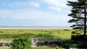 Un jardín con un sendero que lleva a una puerta, diversas plantas y vista a una playa.