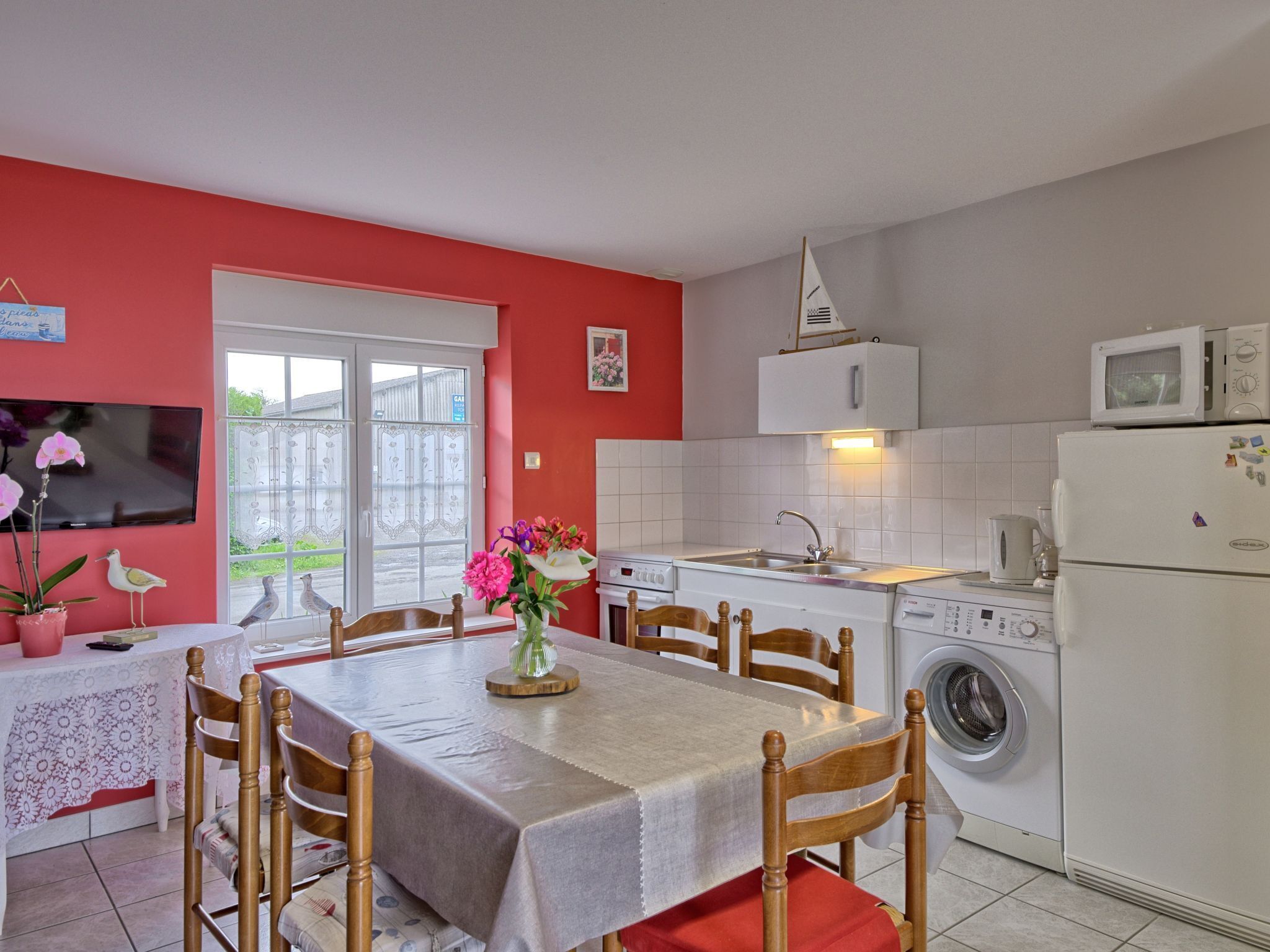 Una cocina compacta con zona de comedor, que incluye una mesa dispuesta para cuatro personas, lavadora y microondas.