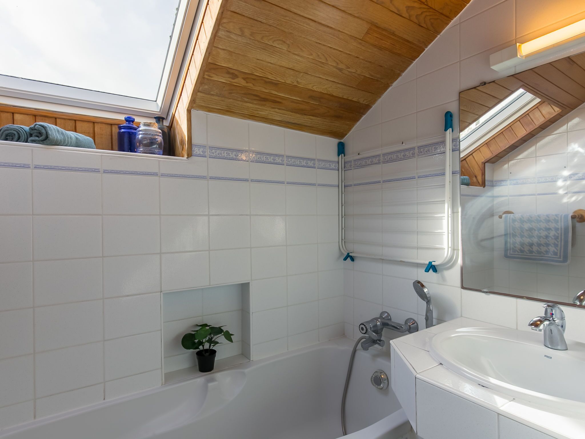 A bathroom with a skylight, a bathtub, a shower, a sink, and a mirror.