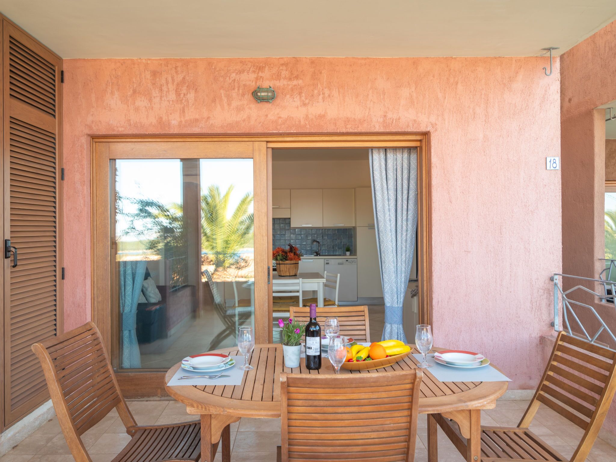 Un coin repas avec une table dressée pour deux personnes, une cuisine visible à travers une porte ouverte et une porte-fenêtre coulissante donnant sur un espace extérieur.