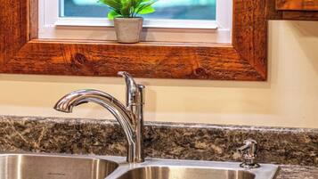 A kitchen with a double stainless steel sink, wooden cabinets, a window with a view of greenery, and a small potted plant on the windowsill.