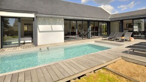 A modern house with a swimming pool, large glass doors, and a deck with lounge chairs. - Villa Noalou by Interhome (Arzon)