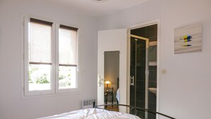 Un dormitorio con cama, ventana, puerta que da a un baño y espejo en la pared.
