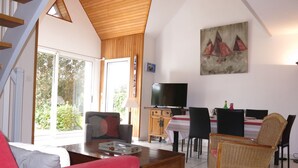 Un amplio salón con techo de madera, una mesa de comedor con sillas, un televisor y un cuadro en la pared.