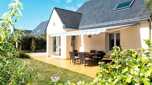 Una casa con patio, zona de estar techada al aire libre y jardín con diversas plantas.