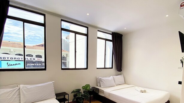 Habitación de hotel con dos camas, una planta en maceta y grandes ventanales con vista a la ciudad.