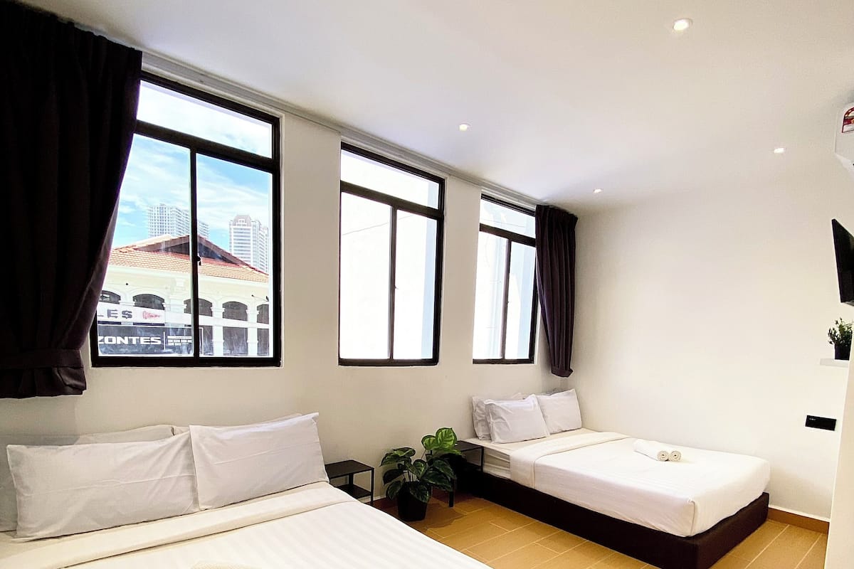 A hotel room with two beds, large windows, and a view of buildings outside.
