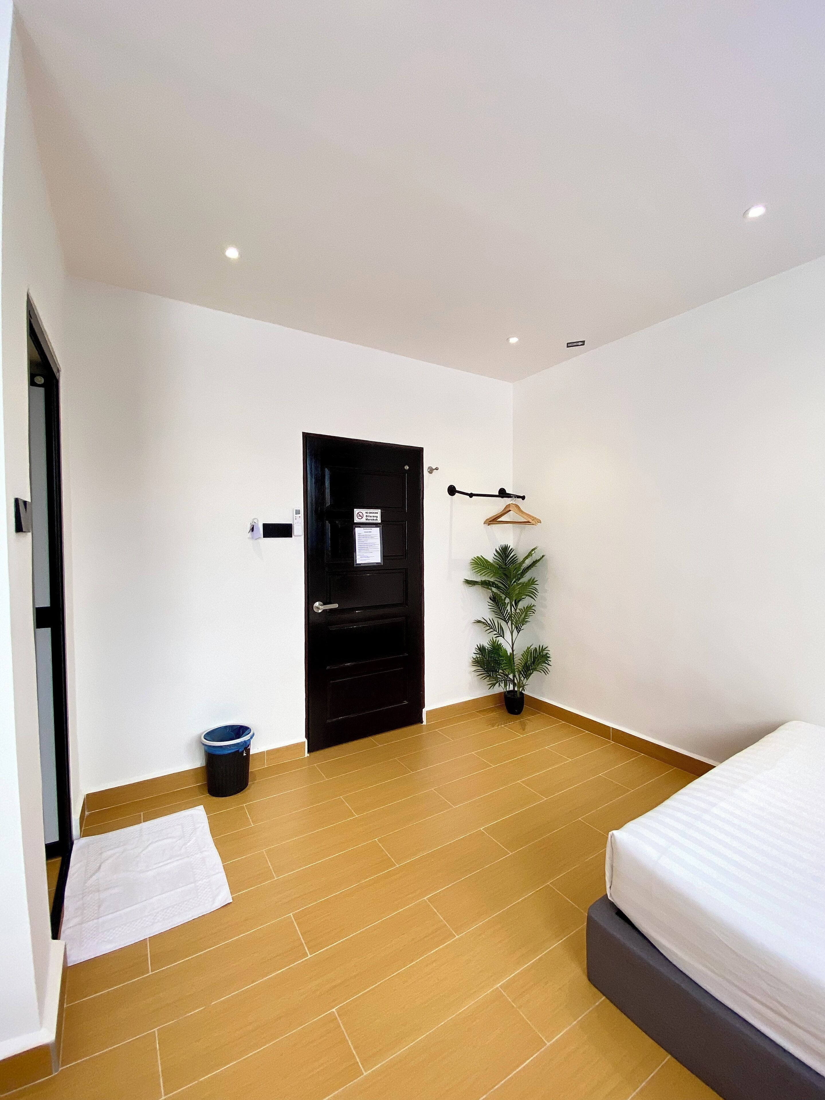 A modern bedroom with a bed, a potted plant, a black door, and a white wall.