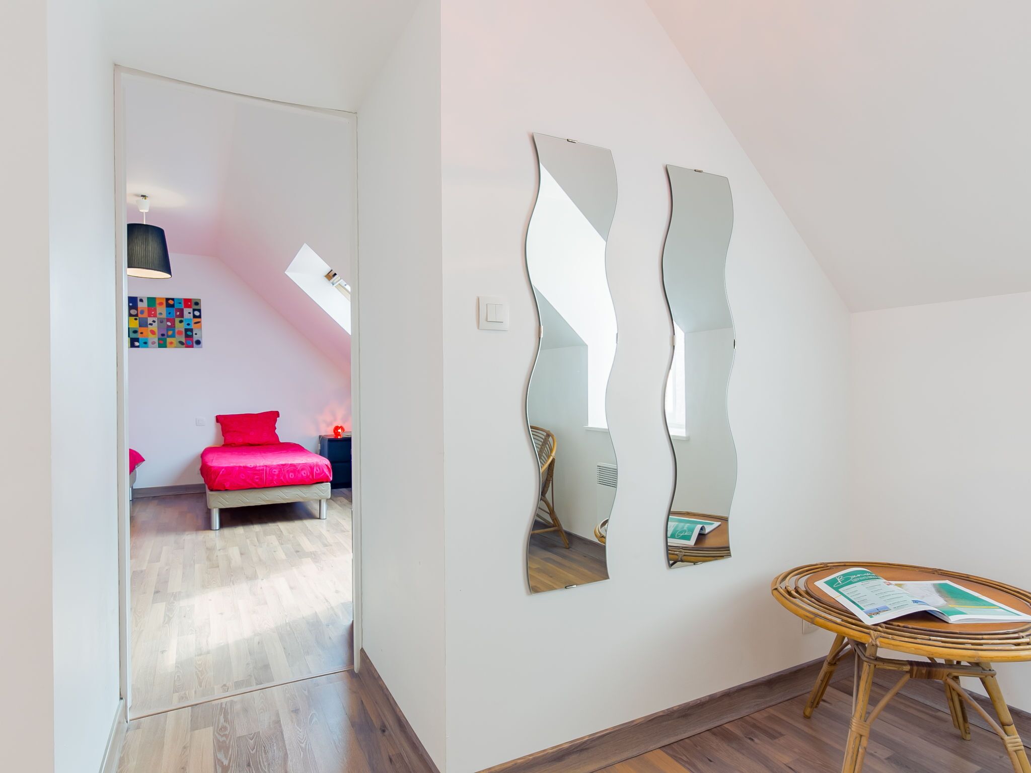A modern room with a bed, a chair, a table with a magazine, and two wall-mounted mirrors.