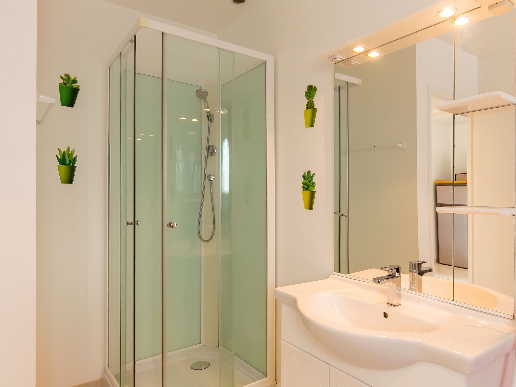 A modern bathroom with a glass-enclosed shower, a white sink, and small potted plants on the walls.