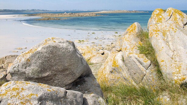 A coastal landscape with large boulders covered in lichen, a sandy beach, and a calm sea. - Les Bambous by Interhome (Guissény)