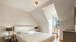 A bedroom with a large bed, a nightstand, a lamp, a wooden chair, and a wardrobe.