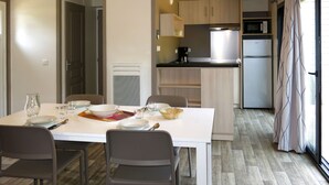 A compact kitchen with a microwave, stove, and refrigerator. There is a dining table with chairs and a white cabinet. - Le Moulin Neuf- 4/6 personnes by Interhome (Rochefort en Terre)