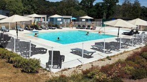 A swimming pool with lounge chairs and umbrellas, surrounded by a fence. - Le Moulin Neuf- 4/6 personnes by Interhome (Rochefort en Terre)