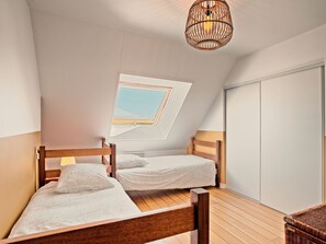 Un dormitorio con dos camas de madera, un tragaluz, una silla de mimbre y un armario.