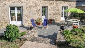 A stone building with a patio area featuring two blue lounge chairs, a table with a green umbrella, and potted plants. - Ty Breiz by Interhome (Ploemeur)