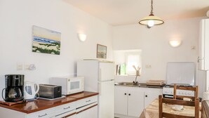 A compact kitchen with white cabinets, a microwave, a coffee maker, and a dining table with chairs. - Ty Breiz by Interhome (Ploemeur)