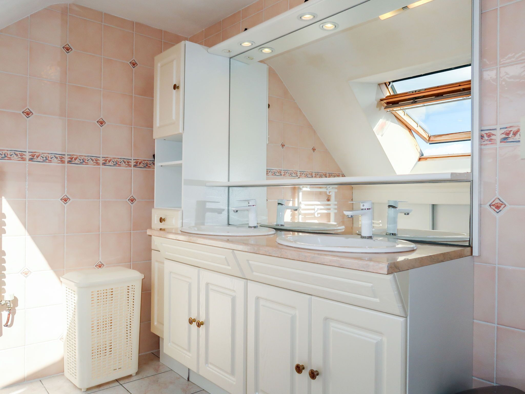 A bathroom with a skylight, two sinks, a mirror, and a white cabinet.