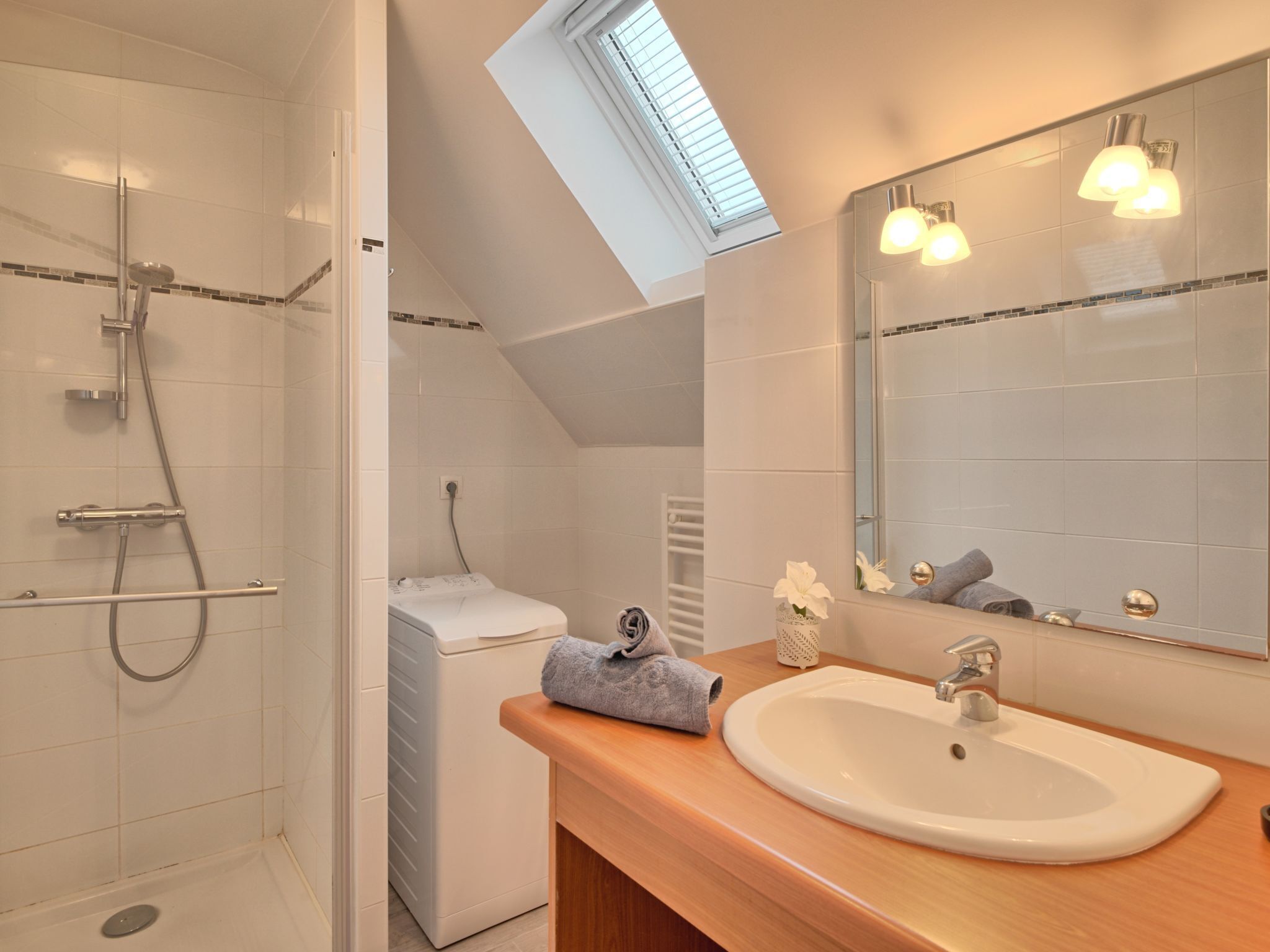 Une salle de bain moderne dotée d’une lucarne, d’une douche à l’italienne, d’un lave-linge encastré, d’un lavabo et d’un grand miroir.