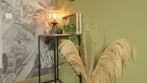 Una stanza con una parete verde, un murale con palme, un quadro incorniciato, un tavolo con una lampada e un vaso con pampas.