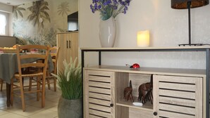 Un coin repas comprenant une table, des chaises, un buffet, un vase avec des fleurs, une bougie et une lampe fixée au mur.