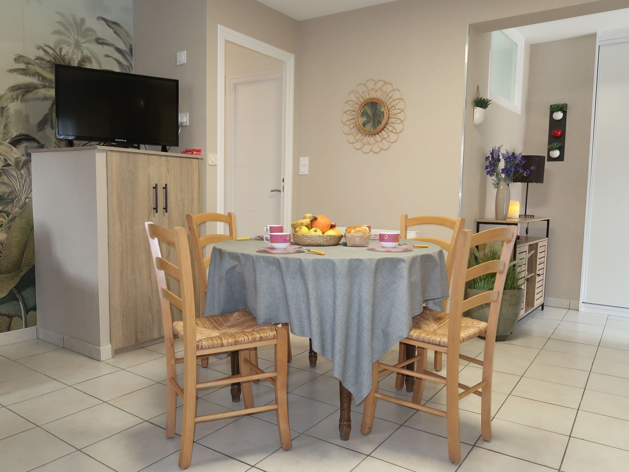 A dining area with a table set for two, surrounded by wooden chairs. A television is mounted on the wall above the table.
