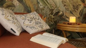 Un coin lecture confortable avec un canapé moelleux, une petite table d’appoint en bois sur laquelle est posée une bougie allumée, et un livre ouvert sur le canapé.