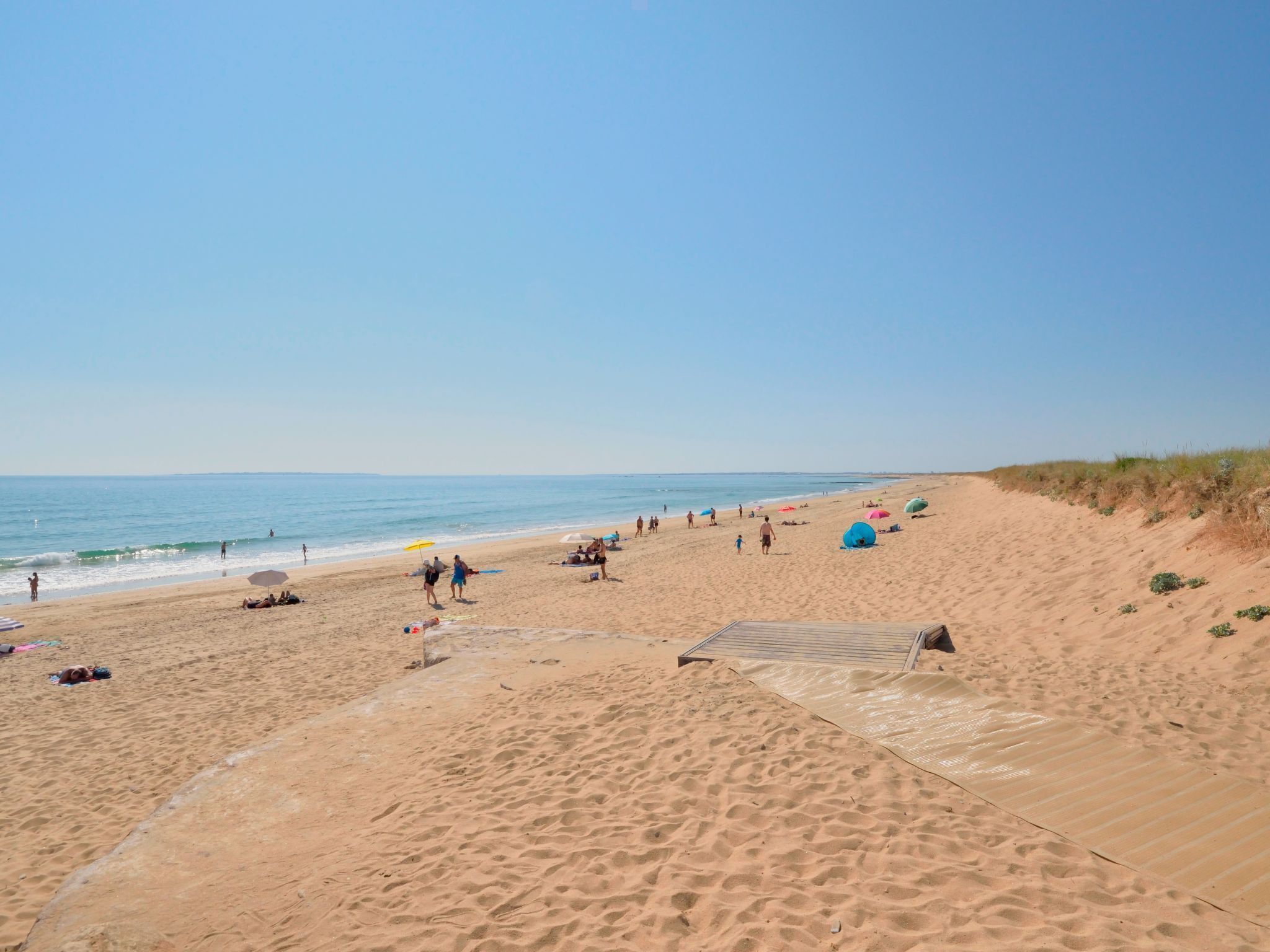 A sandy beach with people, umbrellas, and a wooden boardwalk.