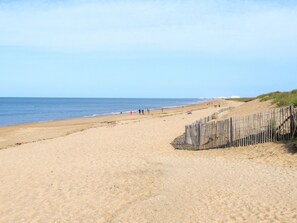 A wide sandy beach with a wooden fence on the right and a clear blue sky. - Hameau Océan by Interhome (Saint Hilaire de Riez)