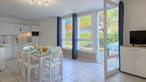 A modern kitchen with white cabinets, a dining table with chairs, and a large window with curtains. - Hameau Océan by Interhome (Saint Hilaire de Riez)
