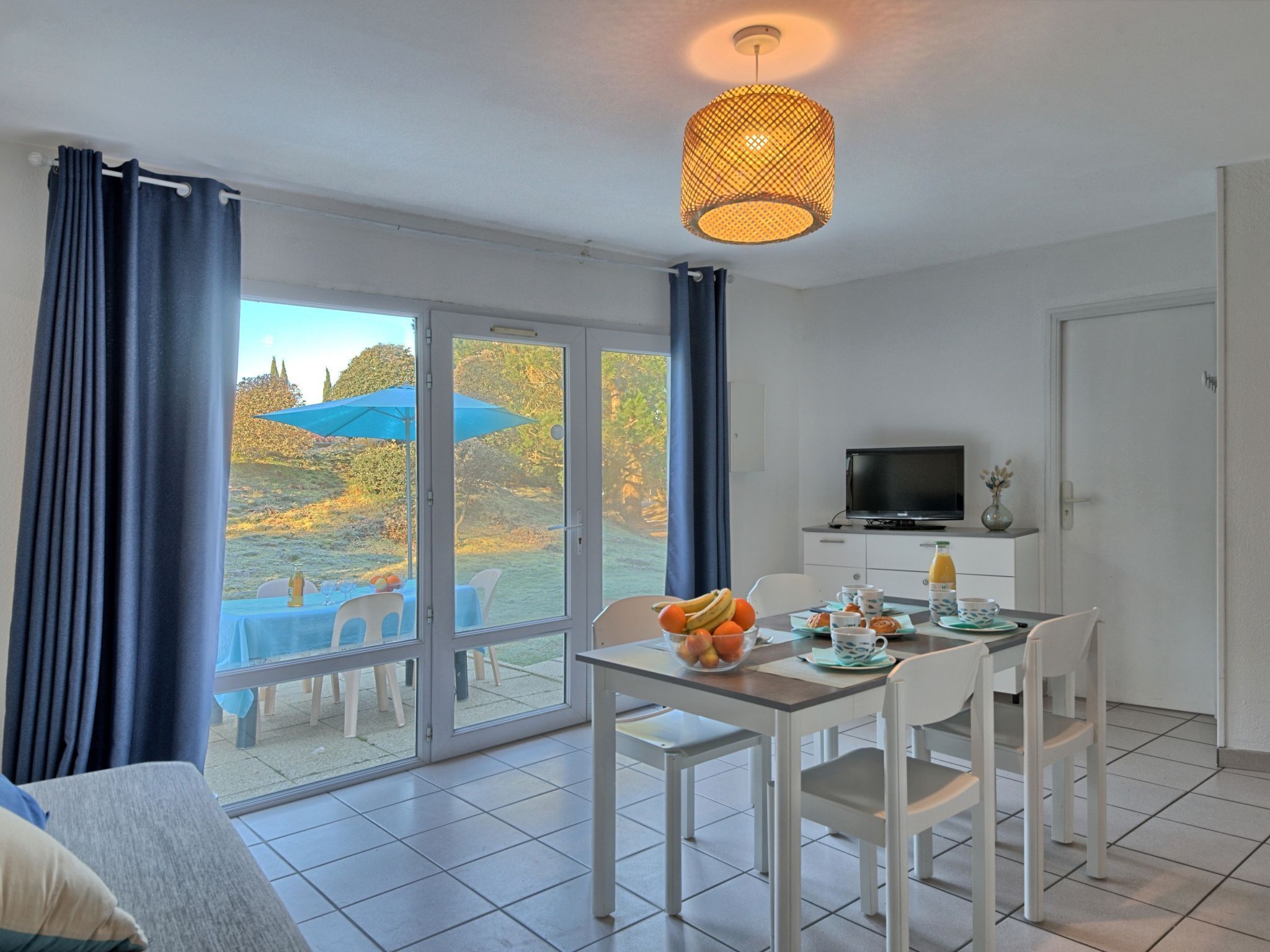 A modern room with a dining area, a TV, and a view of a garden.