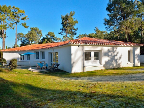 A small, single-story house with a red-tiled roof, a patio with a table and chairs, and a small garden area. - Hameau Océan by Interhome (Saint Hilaire de Riez)